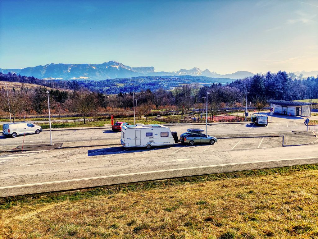 Caravan and car parked on an 'Aire' in France with mountains in the background